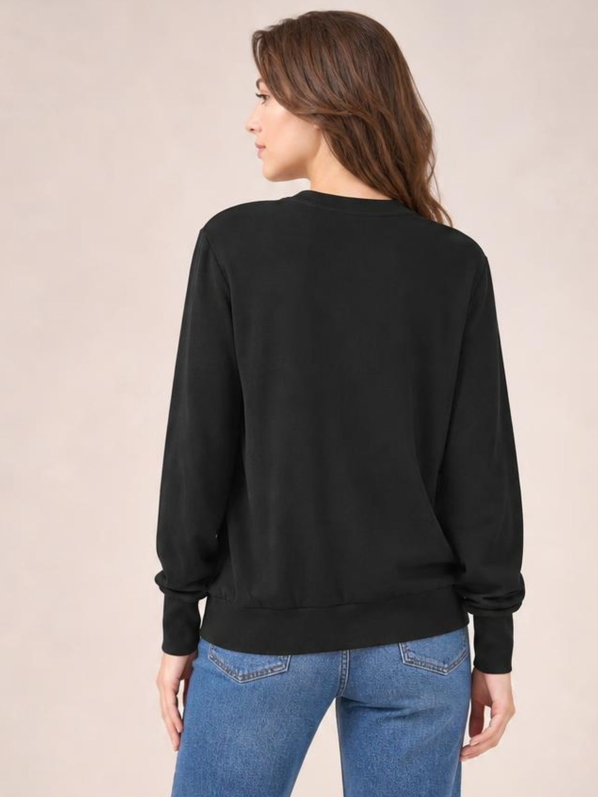 A model stands in a relaxed back-facing pose wearing a black V-neck lantern sleeve top with a loose silhouette, long sleeves, and gathered cuffs.