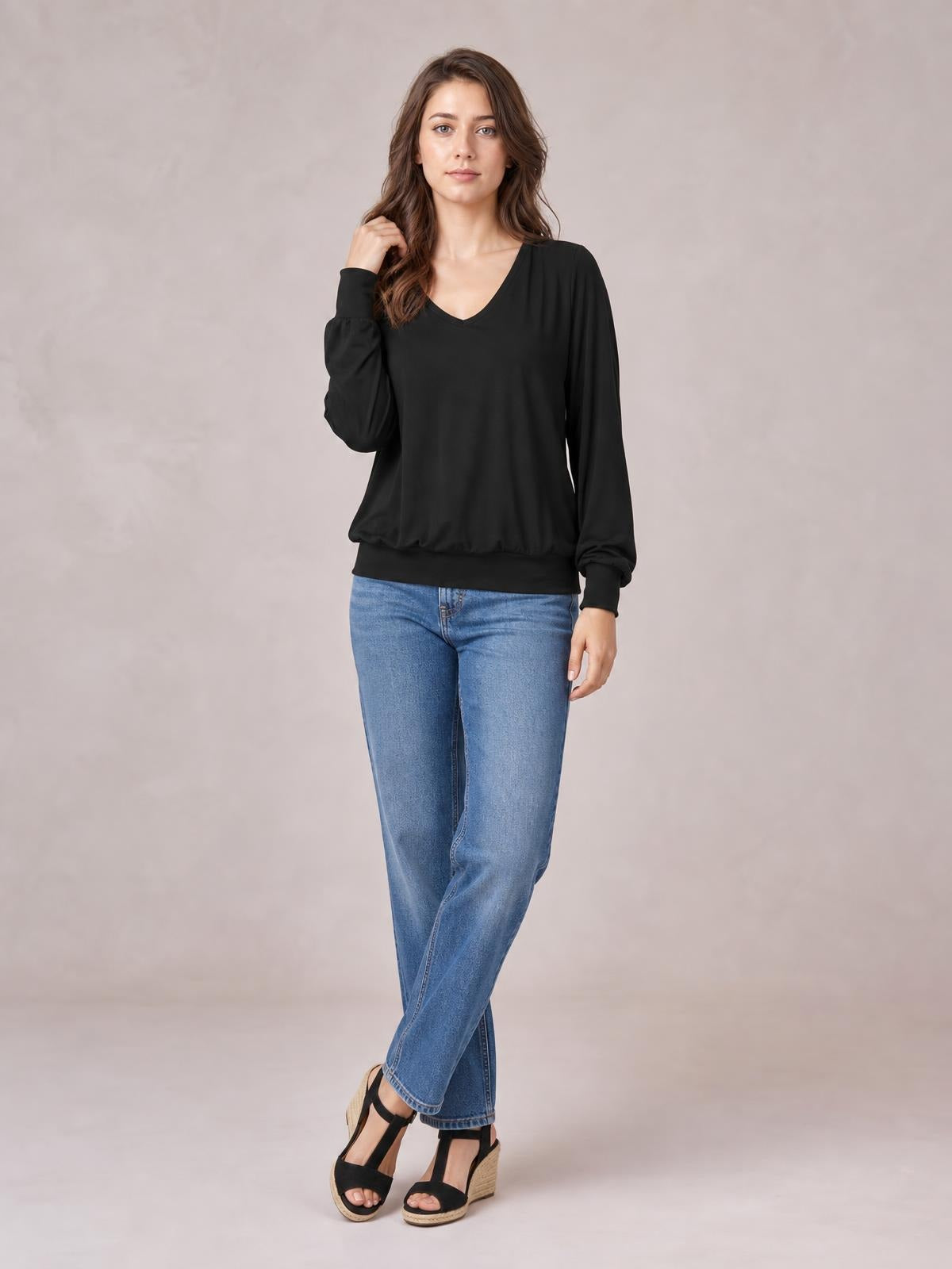 Model in a black V-neck lantern sleeve top with a relaxed silhouette, banded hem and cuffs, posing with one hand in her hair.