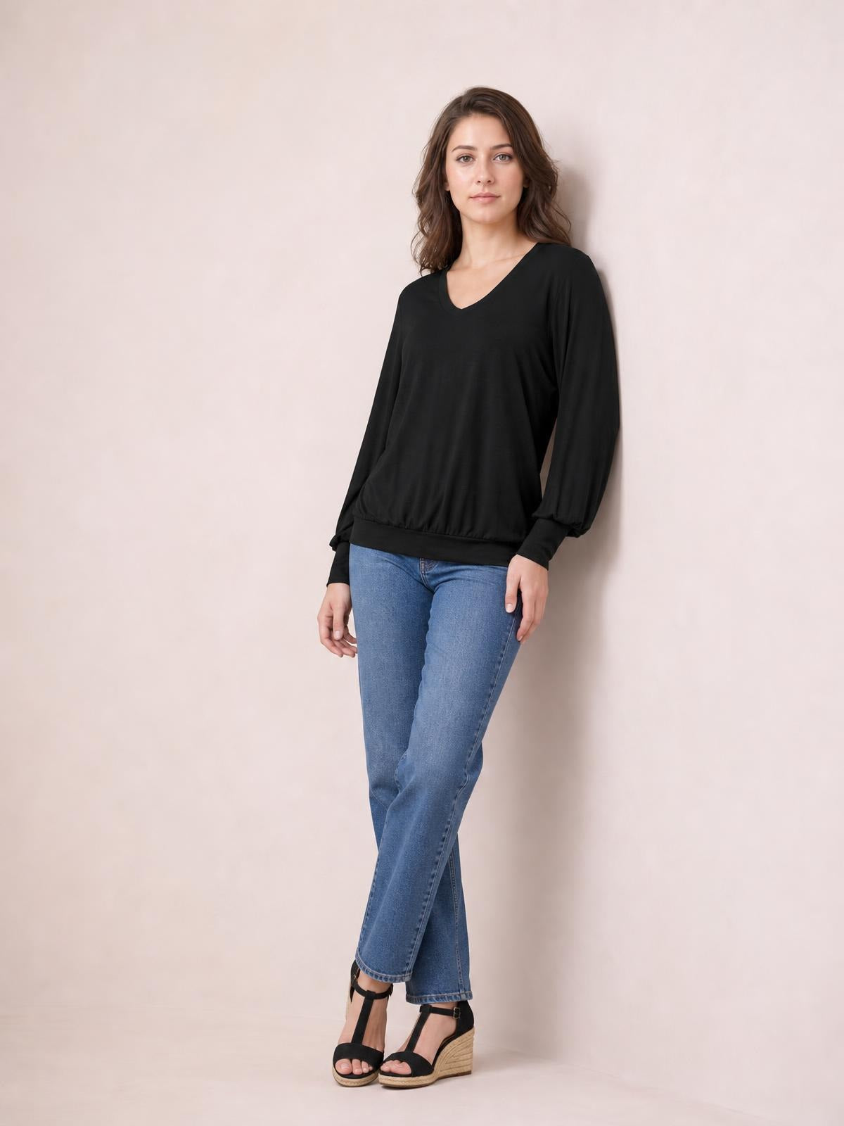 Model poses in a black V-neck lantern sleeve top with a relaxed silhouette, gathered cuffs, and a fitted ribbed hem.