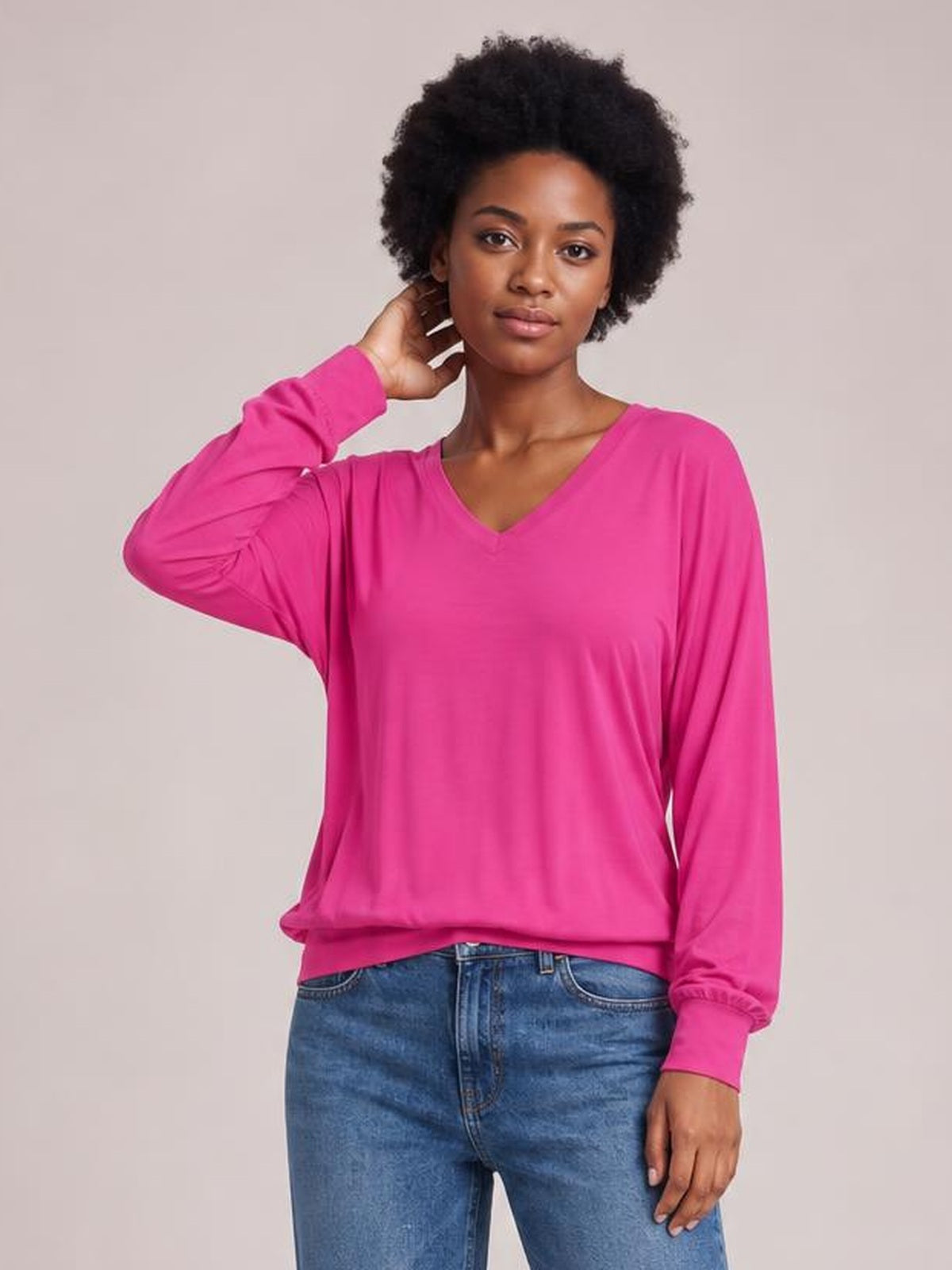 Model poses in a bright pink V-neck top with relaxed silhouette, long lantern sleeves, gathered cuffs, and a slightly loose hem.