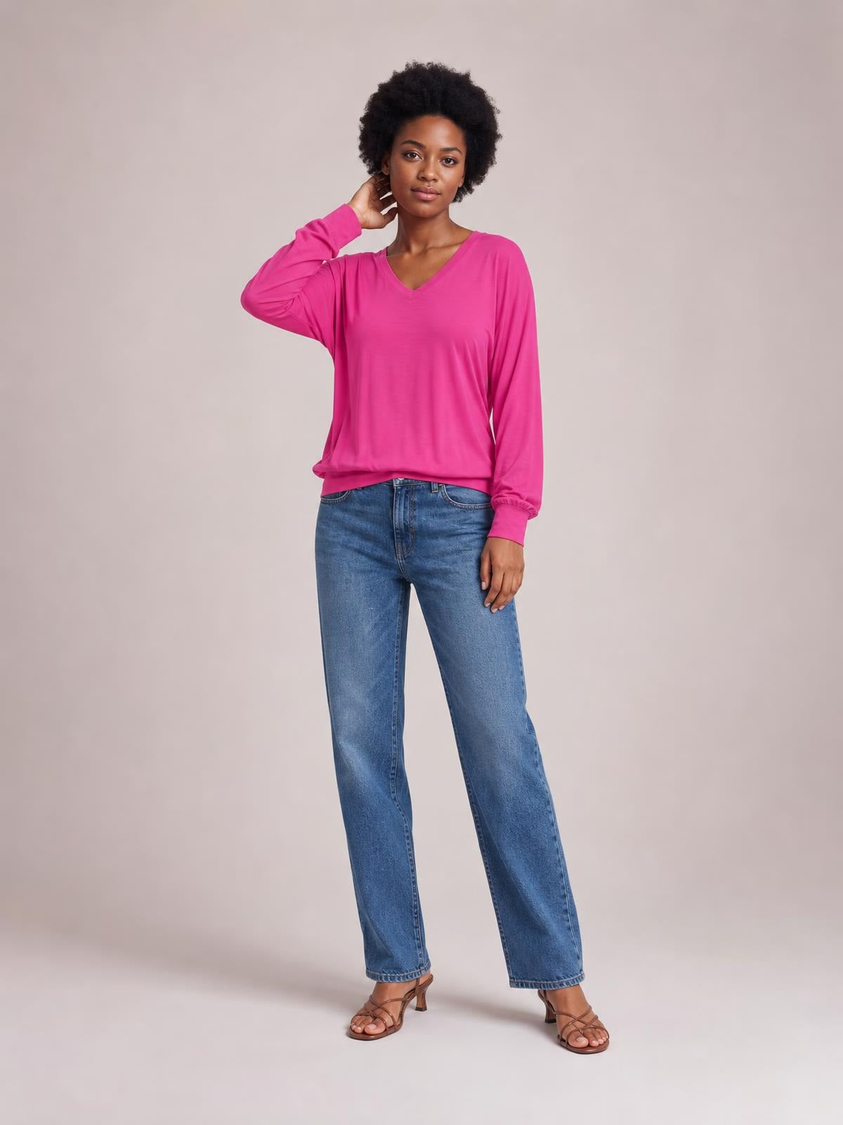 Model poses in a bright pink V-neck lantern sleeve top with a relaxed silhouette, gathered cuffs, and long sleeves, paired with jeans.
