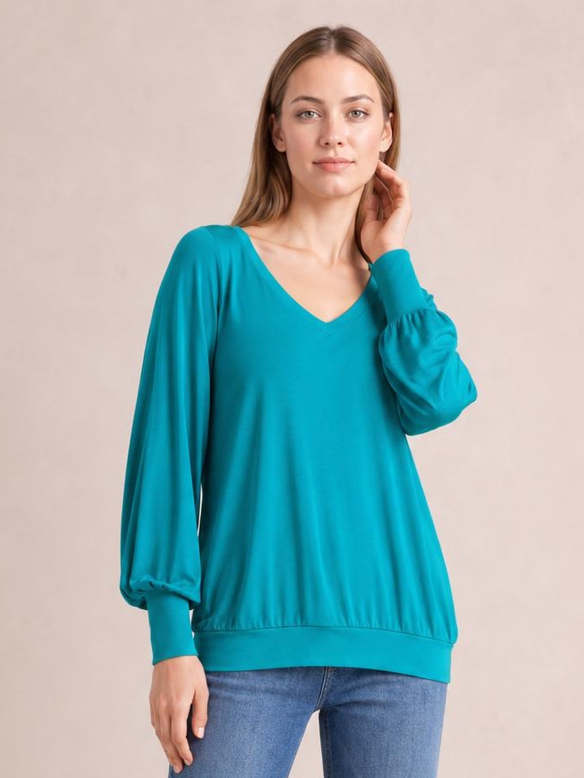 Model poses in a turquoise V-neck lantern sleeve top with a relaxed silhouette, gathered voluminous sleeves, fitted cuffs, and a wide hem band.