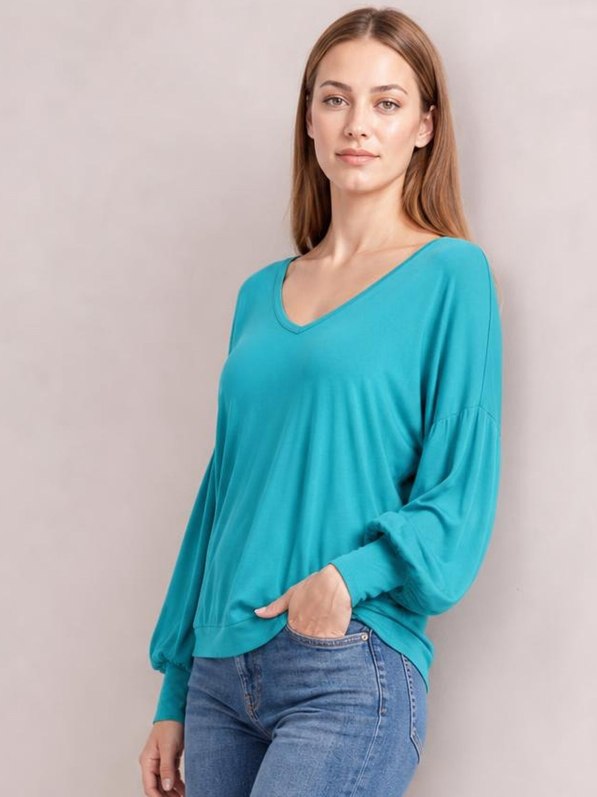 Model poses in a turquoise V-neck top with voluminous lantern sleeves, gathered cuffs, and a relaxed, slightly loose silhouette.
