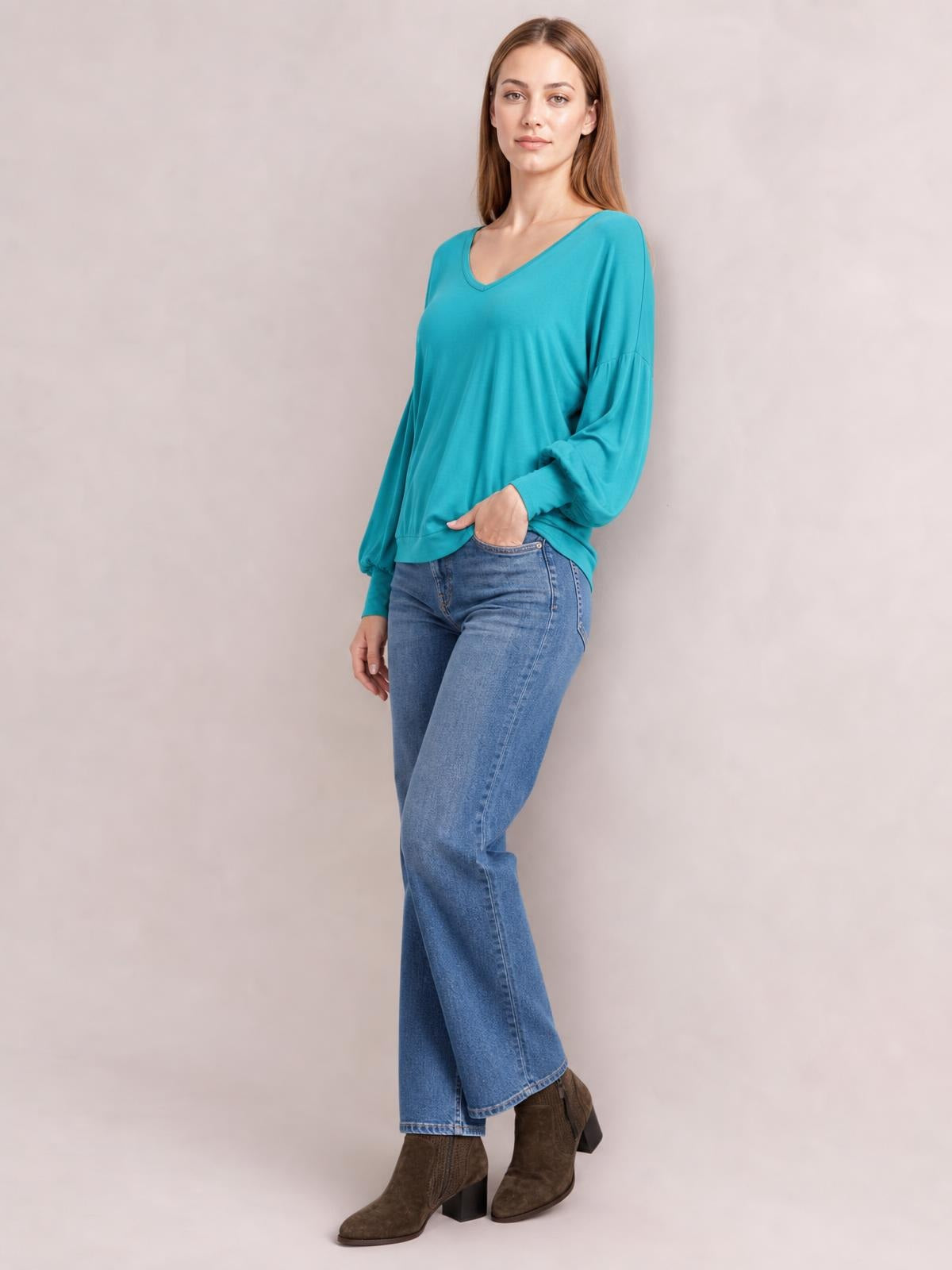 Model poses in a turquoise V-neck lantern sleeve top with voluminous gathered sleeves, ribbed cuffs, and a relaxed slightly draped silhouette.