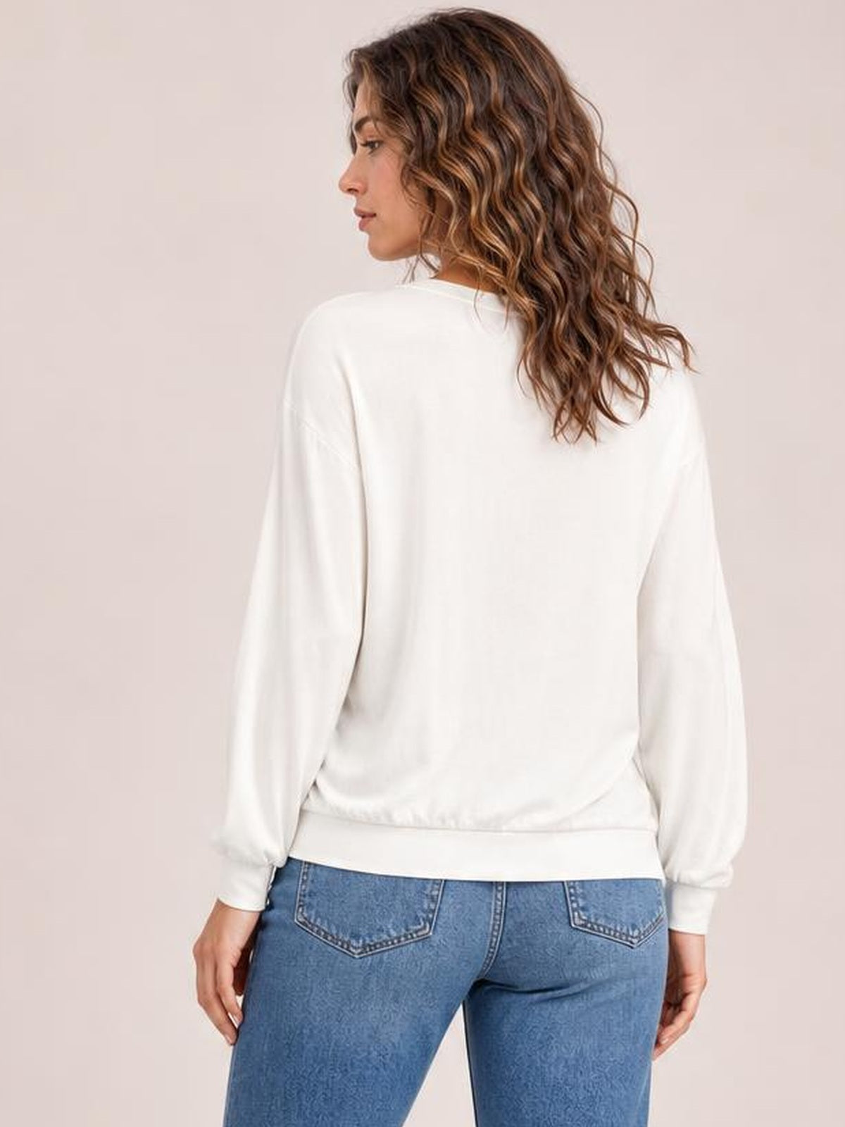 Model shown from the back in a white V-neck top with long lantern sleeves, a relaxed silhouette, and gathered cuffs and hem.