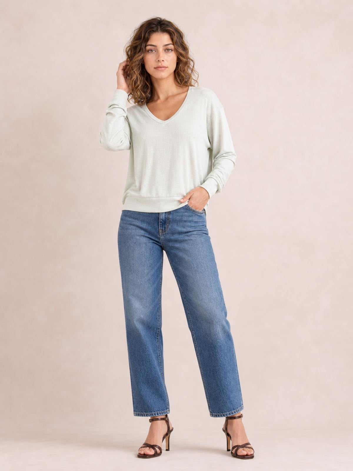 Model wearing an ivory V-neck lantern sleeve top with a relaxed silhouette, long gathered sleeves, and a straight hem, posing with one hand in her jeans pocket.