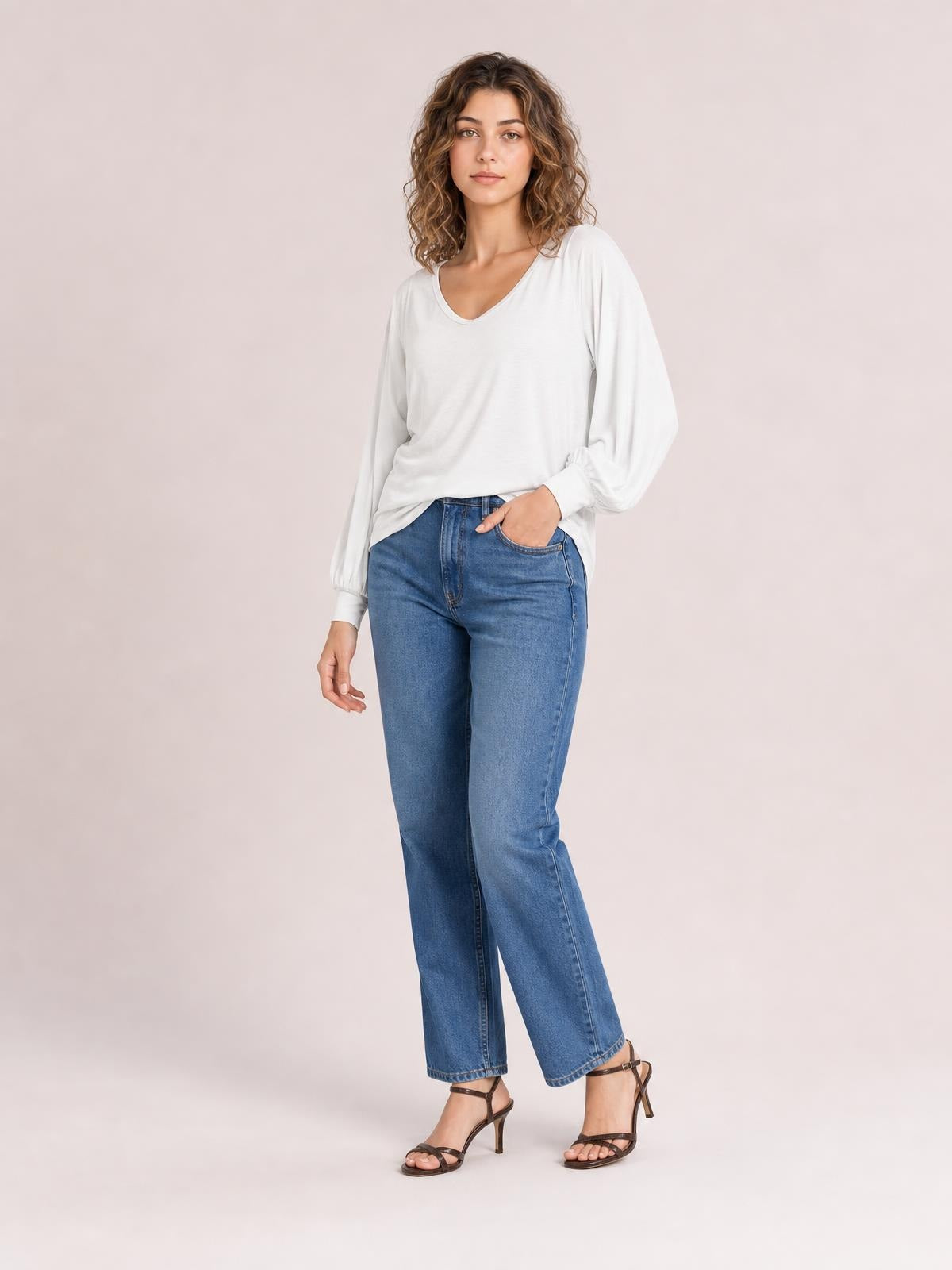 Model poses in a white V-neck lantern sleeve top with gathered cuffs and a relaxed silhouette, paired with blue jeans.