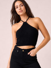 Model poses in a black halter neck ribbed cropped knit top with a fitted silhouette, tied neckline, and exposed midriff.