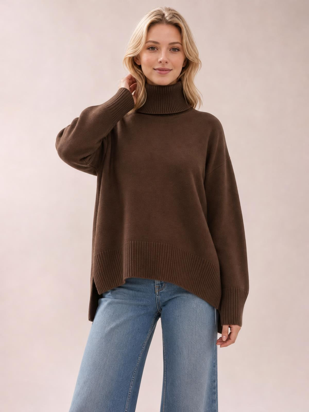 Model wearing a brown turtleneck dropped shoulder long sleeve sweater with a relaxed silhouette, ribbed cuffs and hem, posing with one hand near her neck.