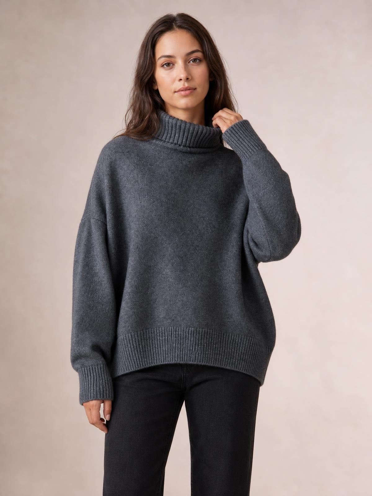 Model wearing a charcoal gray turtleneck sweater with dropped shoulders, long sleeves, ribbed cuffs and hem, and a relaxed oversized silhouette.