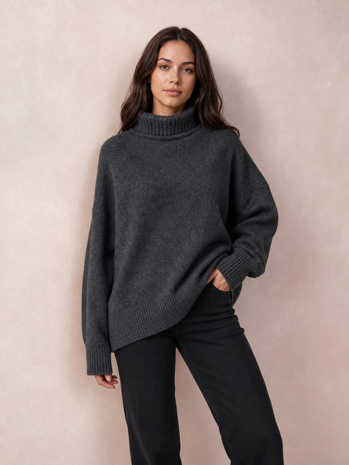 Model wearing a charcoal gray turtleneck sweater with dropped shoulders, long sleeves, ribbed cuffs and hem, and an oversized relaxed silhouette.