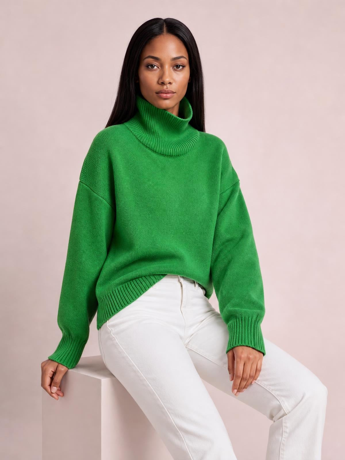 Model seated in a bright green turtleneck dropped-shoulder sweater with long sleeves, ribbed cuffs and hem, and a relaxed oversized silhouette.