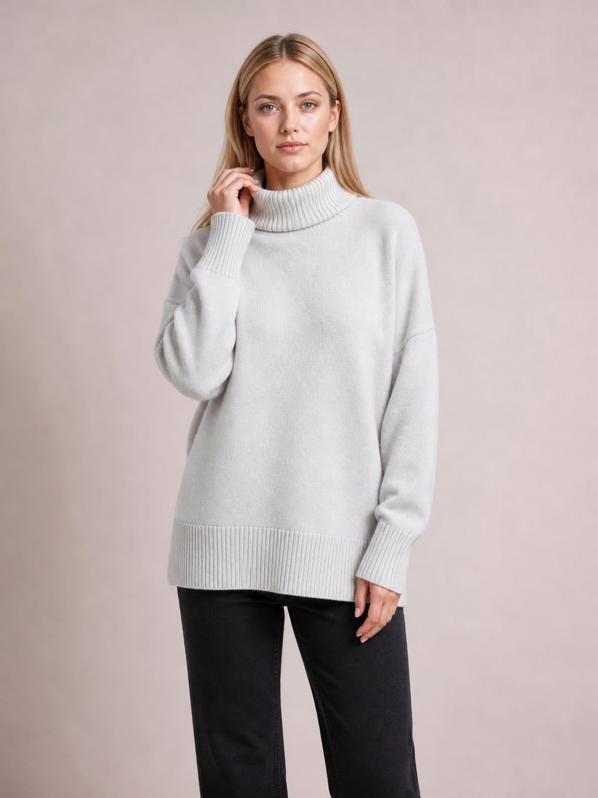 Model wearing a light gray turtleneck dropped shoulder long sleeve sweater with an oversized silhouette, ribbed cuffs, collar, and hem.