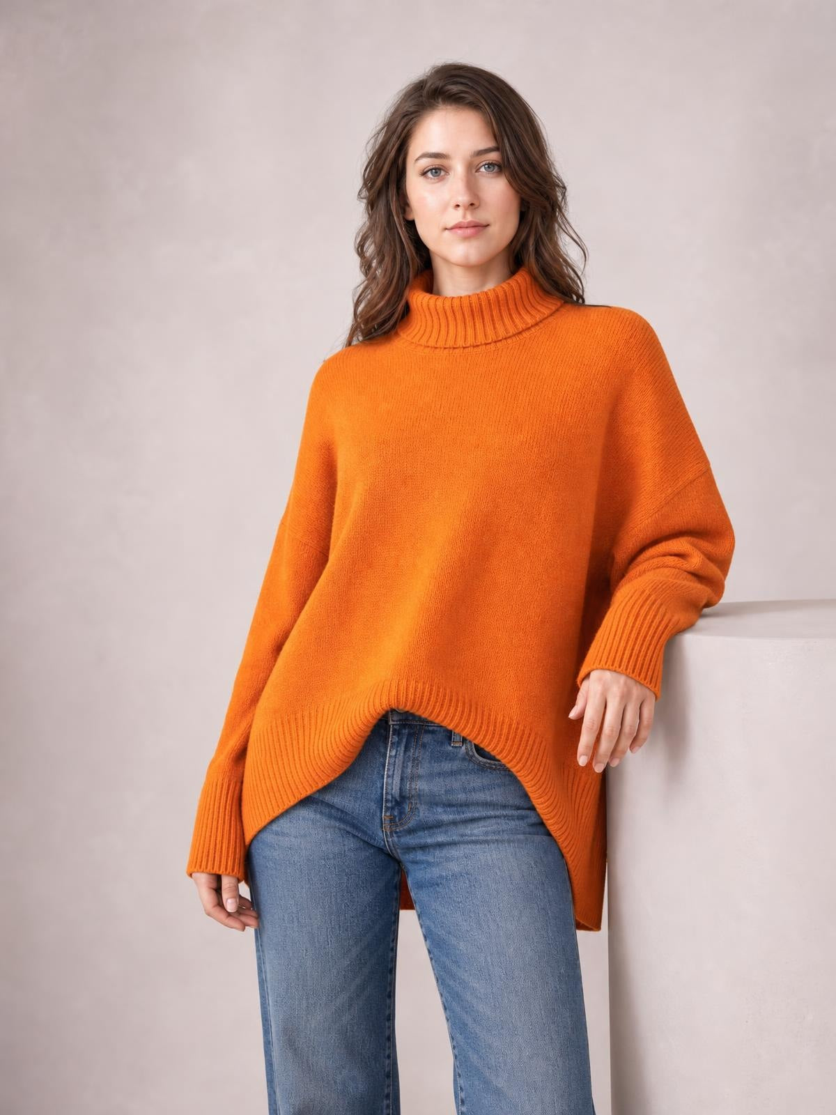 Model wears an orange turtleneck dropped-shoulder long-sleeve sweater with an oversized silhouette, ribbed cuffs and hem, standing in blue jeans.