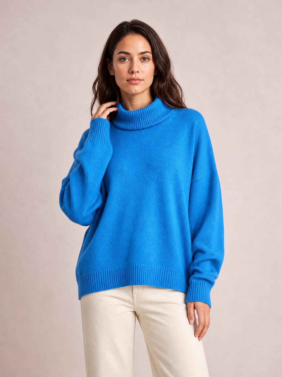Model touching her hair while wearing a bright blue turtleneck dropped-shoulder long sleeve sweater with an oversized silhouette and ribbed cuffs and hem.