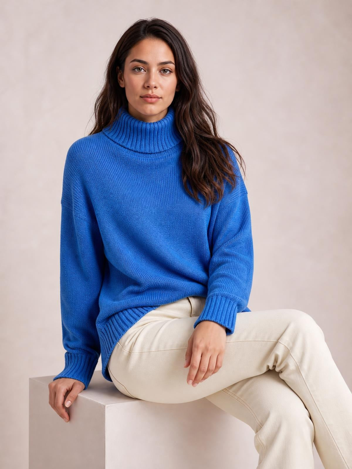 A model sits in a bright blue turtleneck dropped-shoulder sweater with long sleeves, ribbed cuffs and hem, and a relaxed silhouette.