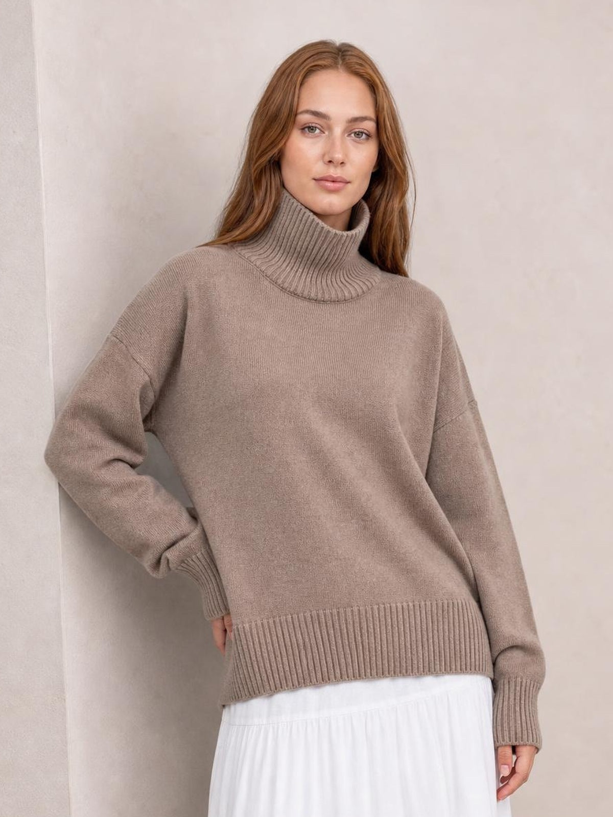Model wearing a taupe turtleneck dropped-shoulder sweater with long sleeves, ribbed neckline, cuffs, and hem in a relaxed silhouette.