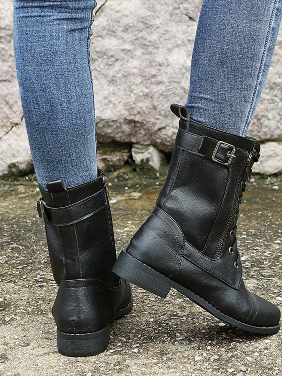 A model wears black PU leather lace-up boots with side zippers, buckle straps, panelled construction, rounded toes, and low heels over blue jeans.