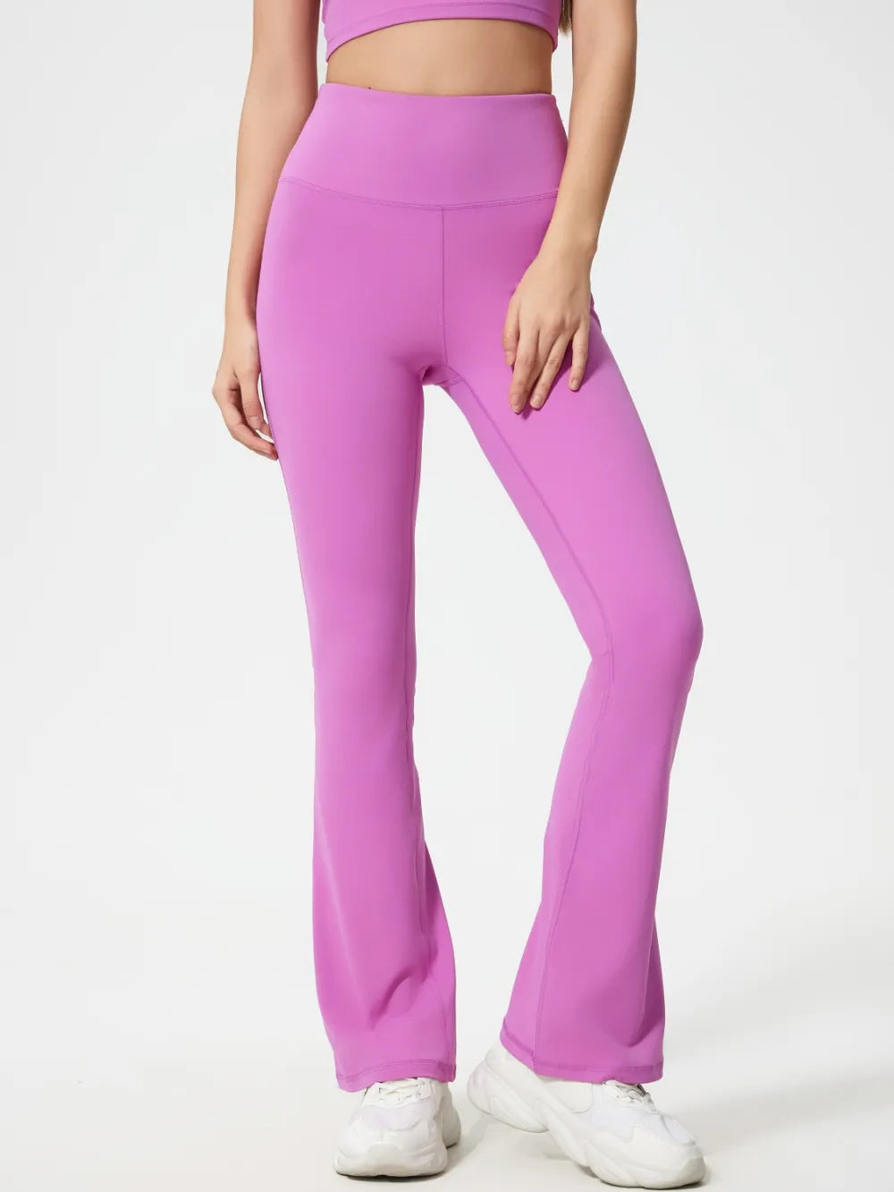 Model wearing bright pink high waist active pants with a smooth, stretchy fit, seamed construction, and flared legs, standing with one knee bent.