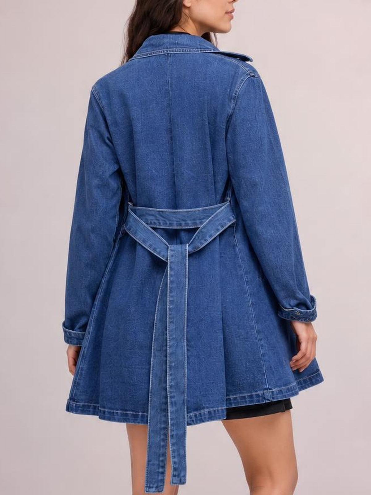 Model shown from behind wearing a blue belted denim jacket with long sleeves, rolled cuffs, seam detailing, and a flared, hip-length silhouette.