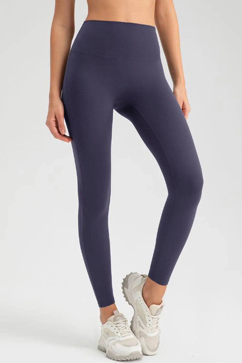 Model poses in dark navy high-waist skinny active pants with a smooth wide waistband, stretch fit, tapered full-length legs, and minimal seaming.