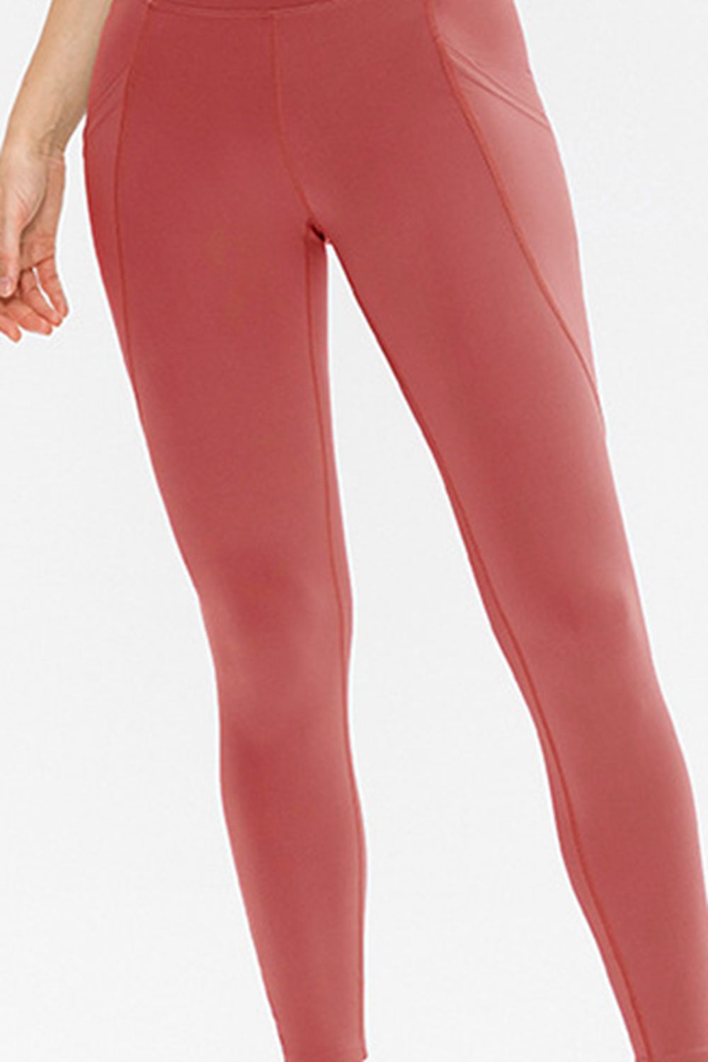 A model stands with legs slightly apart, showcasing solid coral-red slim-fit active leggings with a long silhouette, stretch construction, and a visible side pocket.