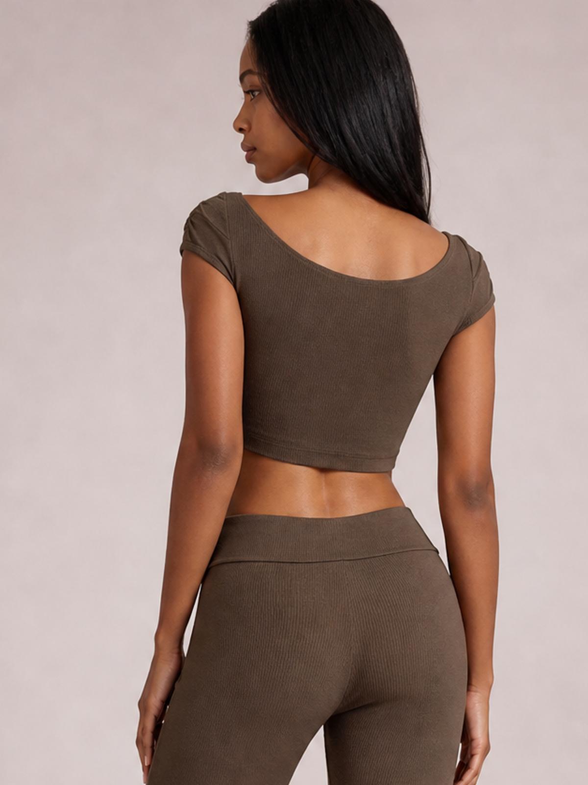 A model poses turned away in a chocolate boat neck cap sleeve top with a cropped silhouette and matching high-waisted pants in a streamlined set.