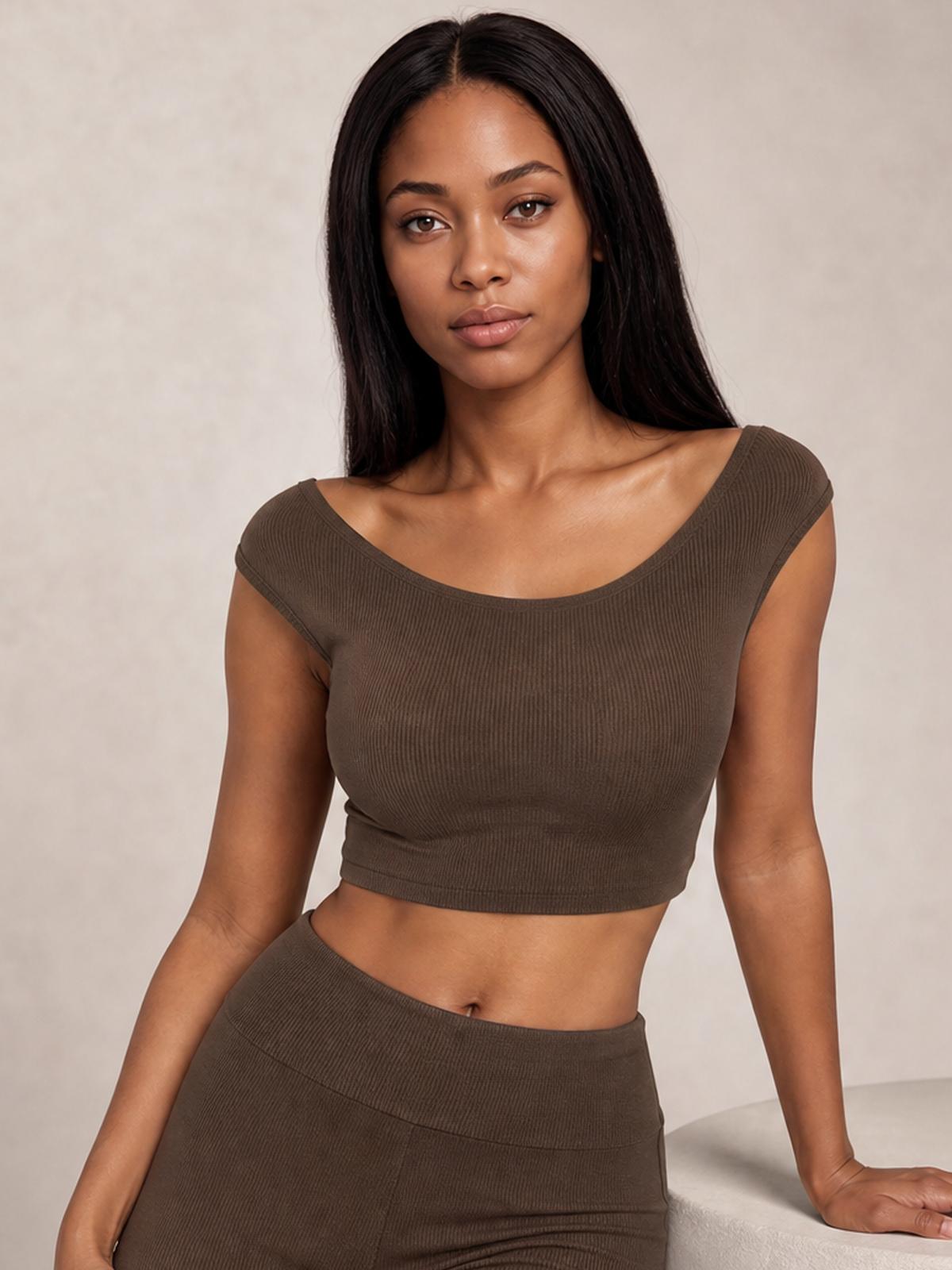 A model leans seated wearing a chocolate boat neck cap sleeve top and matching high-waisted pants in a fitted, ribbed silhouette.