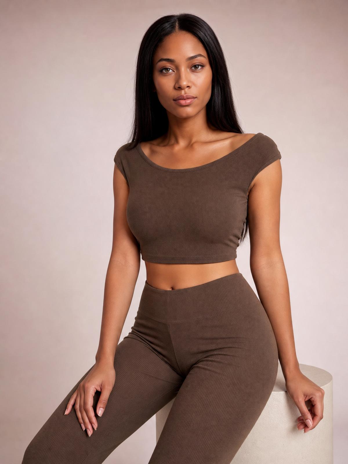 A seated model wears a chocolate boat neck cap sleeve top with a cropped fitted silhouette and matching high-waisted ribbed pants.