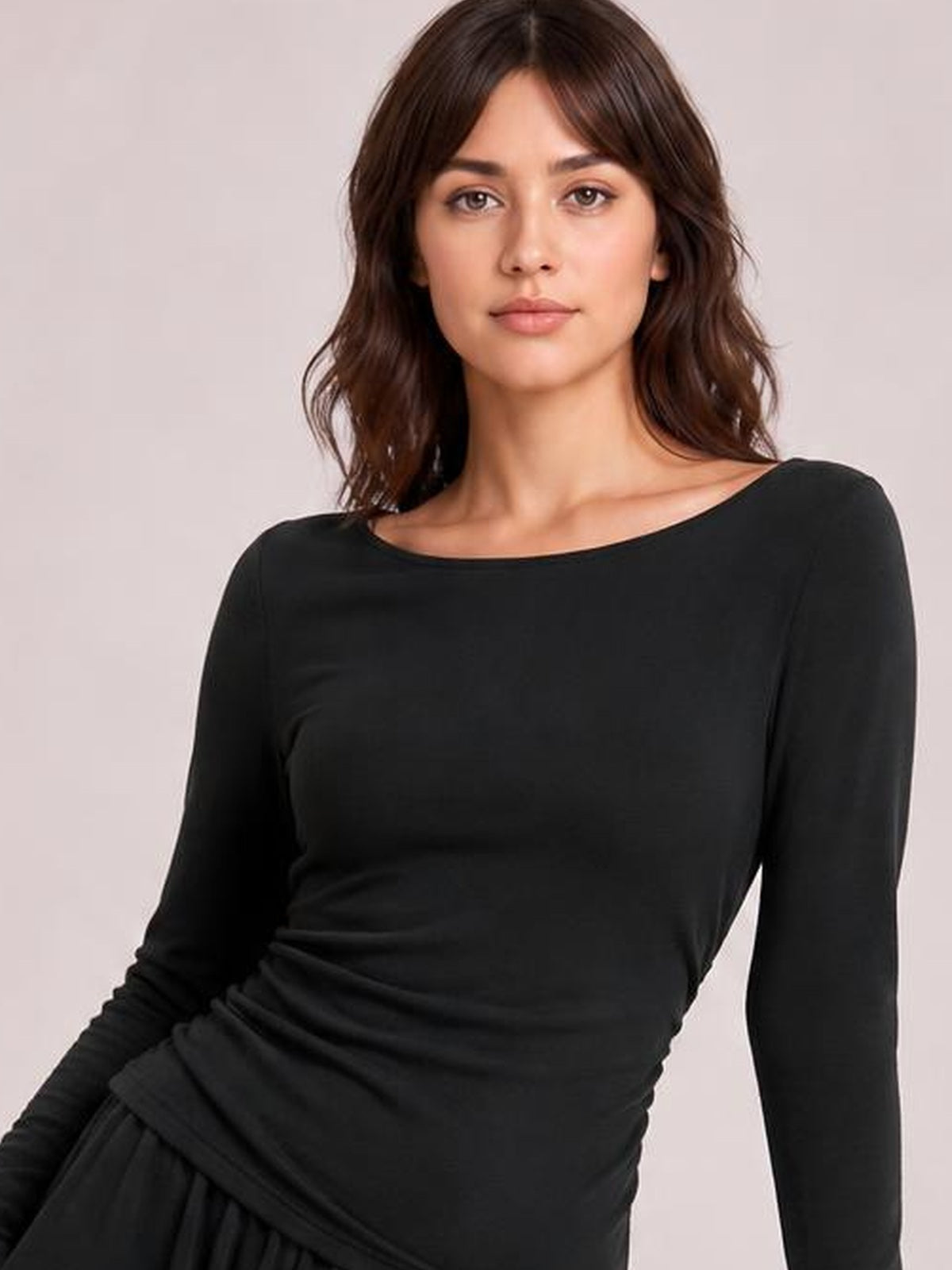 Model poses in a black boat-neck long-sleeve top with a smooth, close-fitting silhouette and softly gathered draping at the waist.