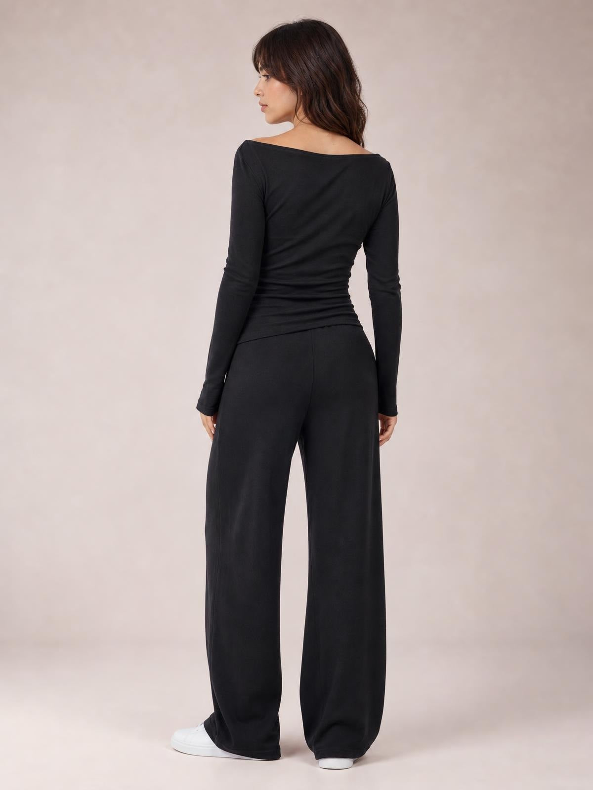 Model turned slightly away wears a black boat-neck long-sleeve top and coordinating wide-leg pants set with a relaxed, flowing silhouette.