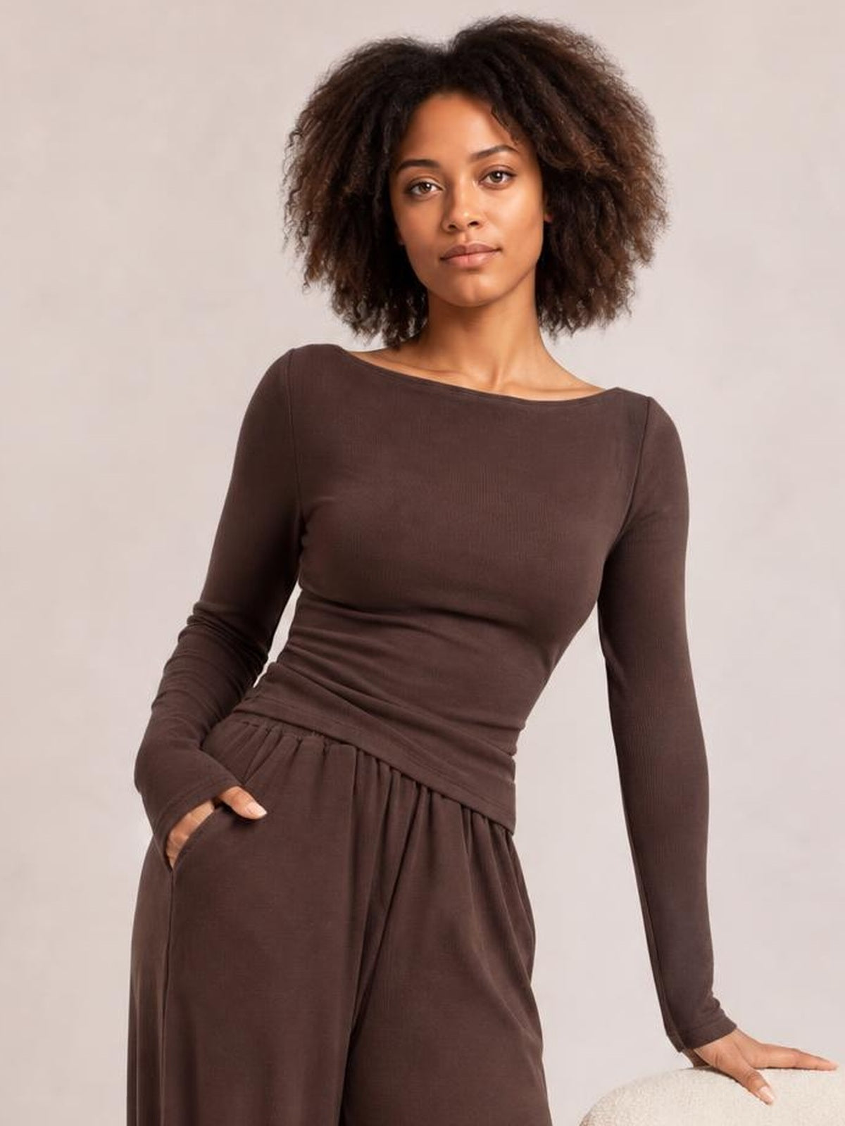 A model poses in a brown boat-neck long-sleeve top and coordinating relaxed pants, showing the fitted silhouette, gathered waistband, and practical pocket.