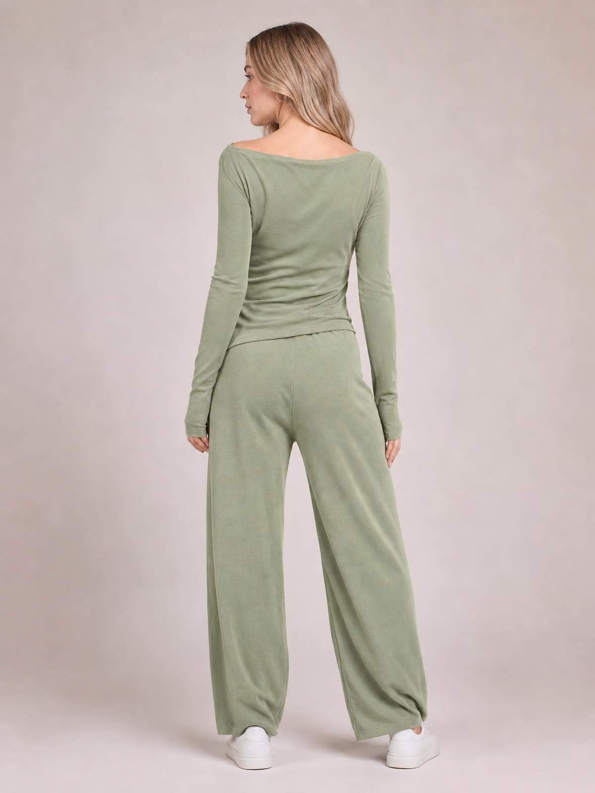 A model poses from behind in a sage green boat-neck long-sleeve top and coordinating wide-leg pants, turning her head over one shoulder.