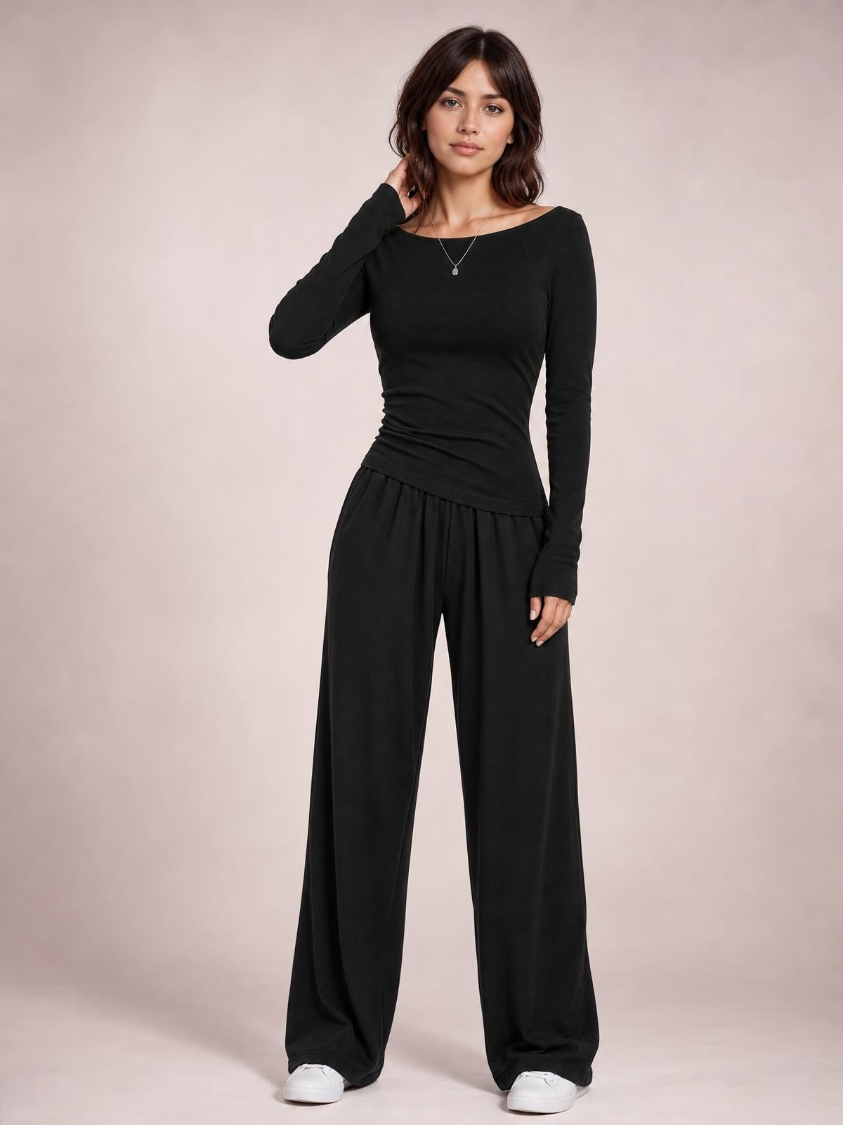 Model poses in a black boat-neck long-sleeve top and coordinating wide-leg pants set, with a fitted silhouette and one hand touching her hair.