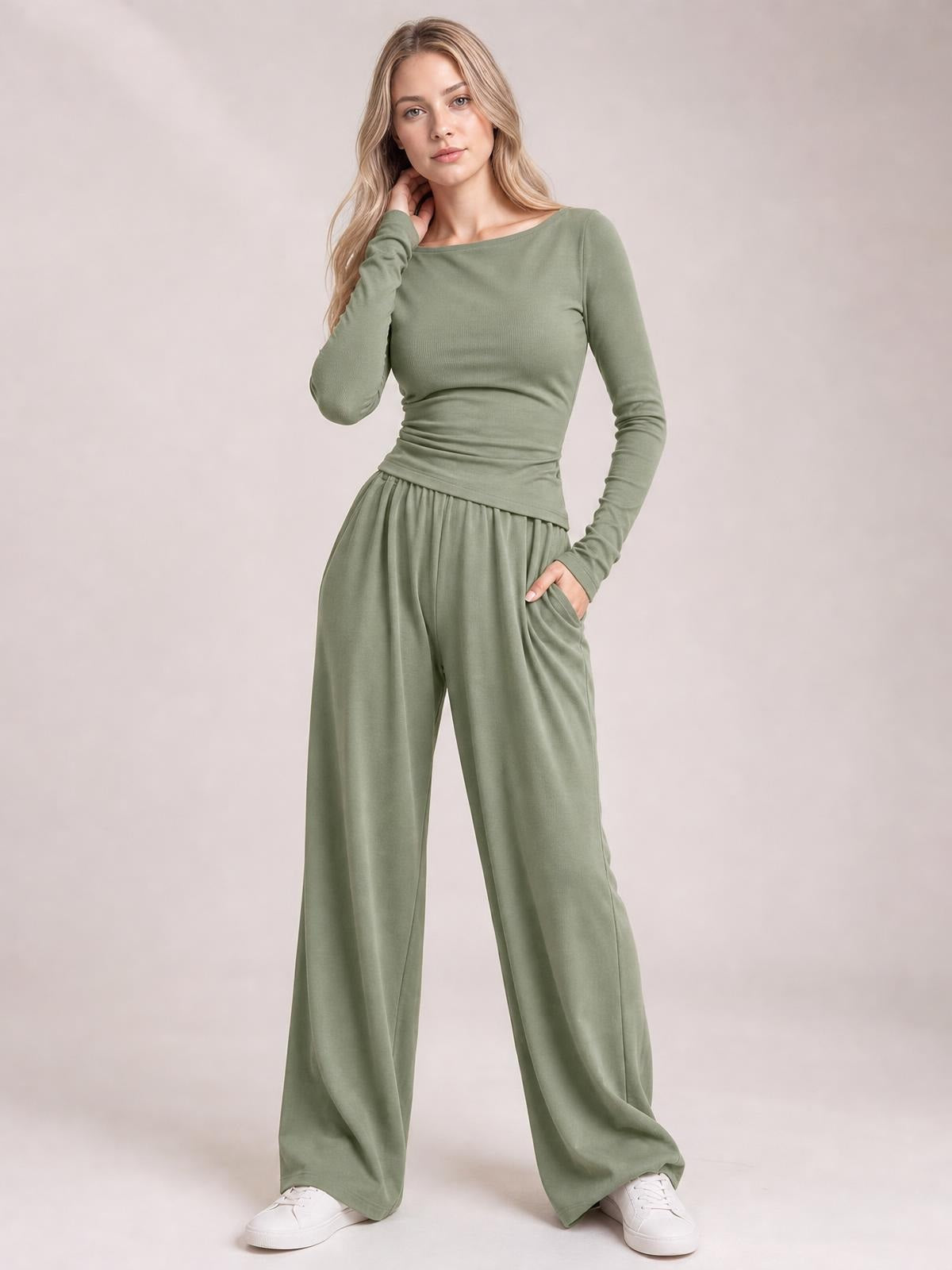 A model poses in a sage green boat-neck long-sleeve top with a fitted, gently ruched waist and coordinating wide-leg pants with a side pocket.