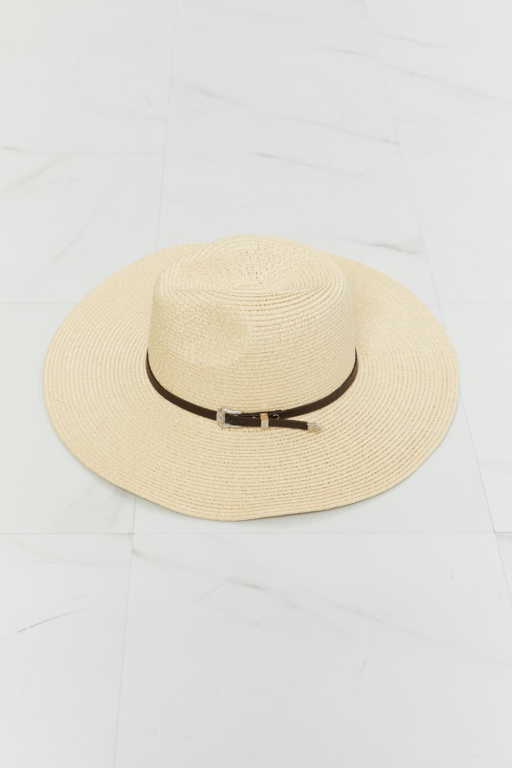 Ivory woven straw fedora with a softly structured crown, wide brim, contrasting dark band, and small metallic buckle detail.