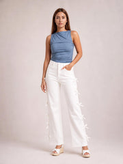 Model poses with one hand in the pocket of white bow-accented wide-leg pants, featuring a high-rise waist and bows along the outer legs.