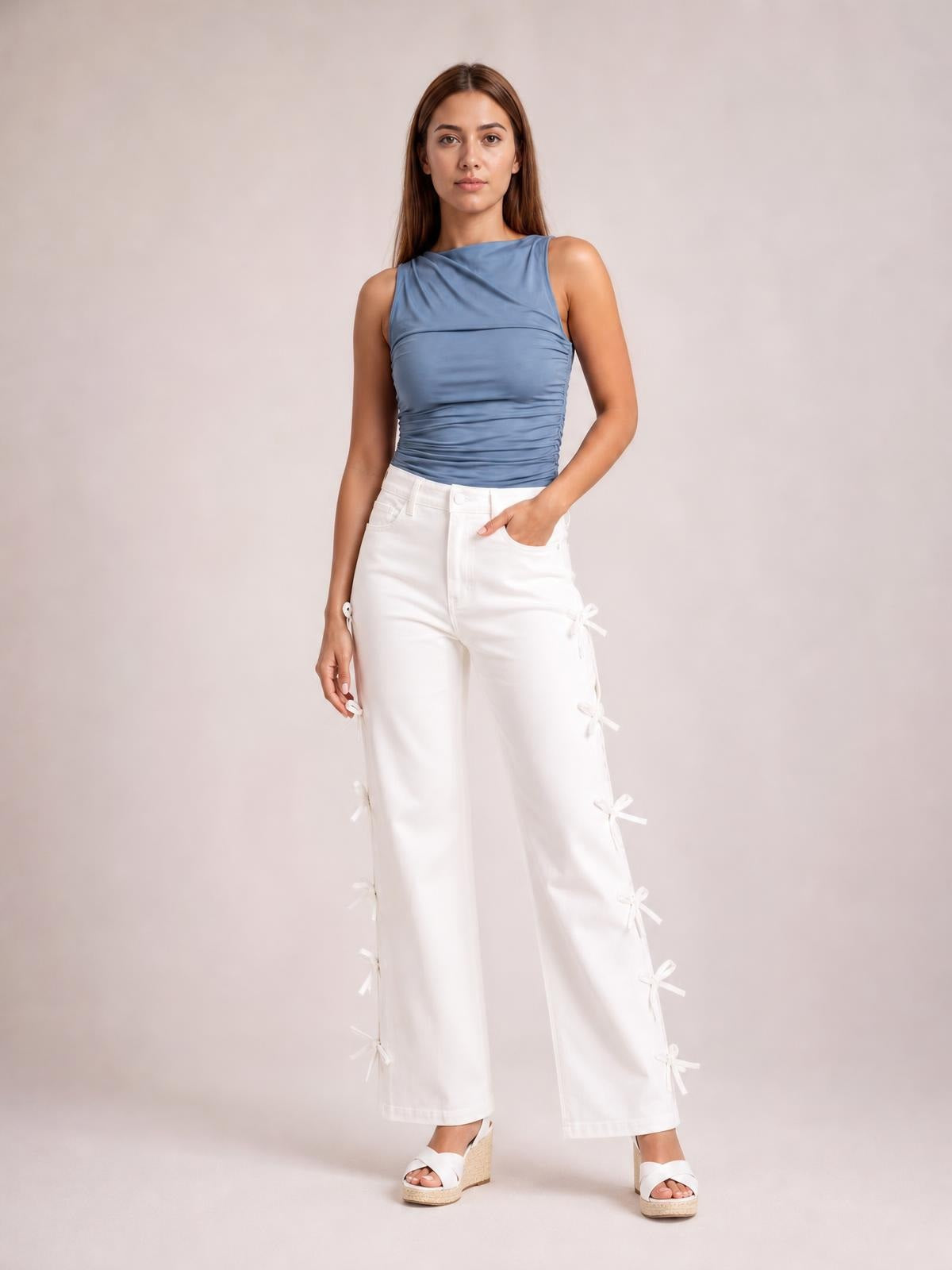 Model poses with one hand in the pocket of white bow-accented wide-leg pants, featuring a high-rise waist and bows along the outer legs.