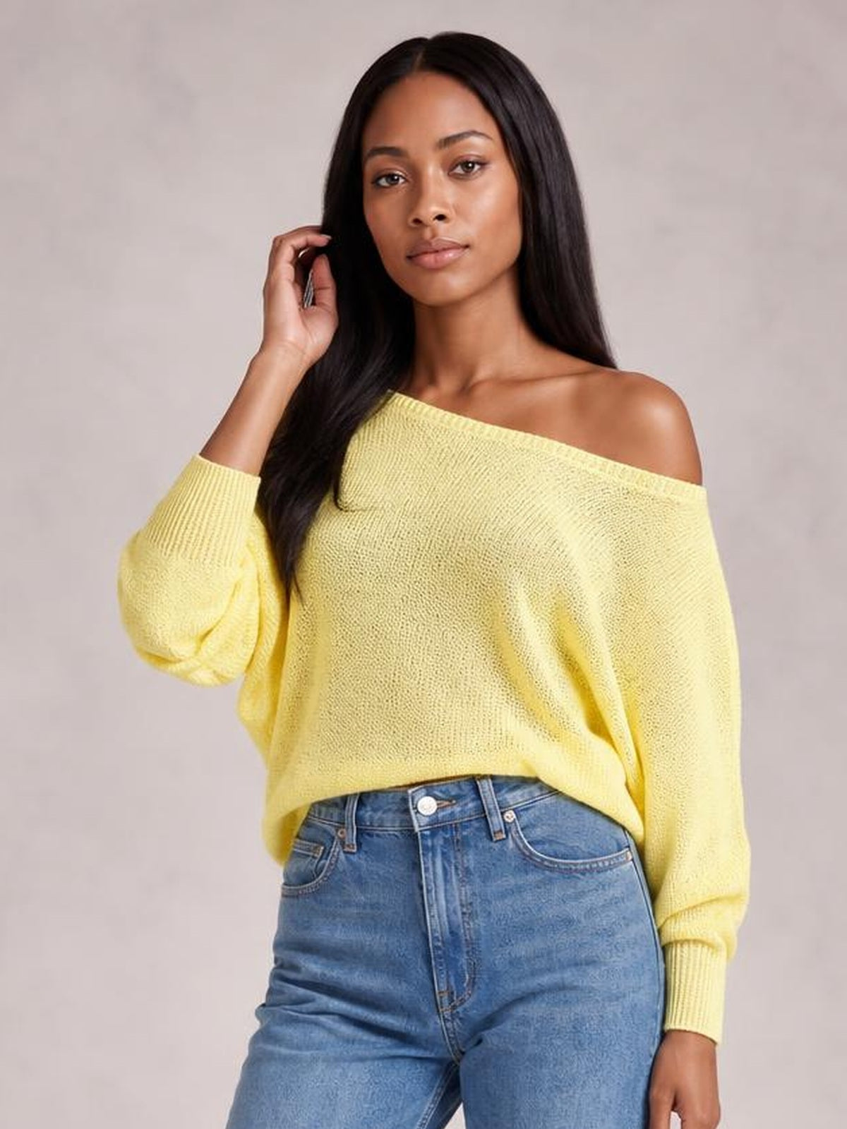 Model wearing a pale yellow boat-neck sweater with loose batwing sleeves and a relaxed silhouette, posing with one hand touching her hair.