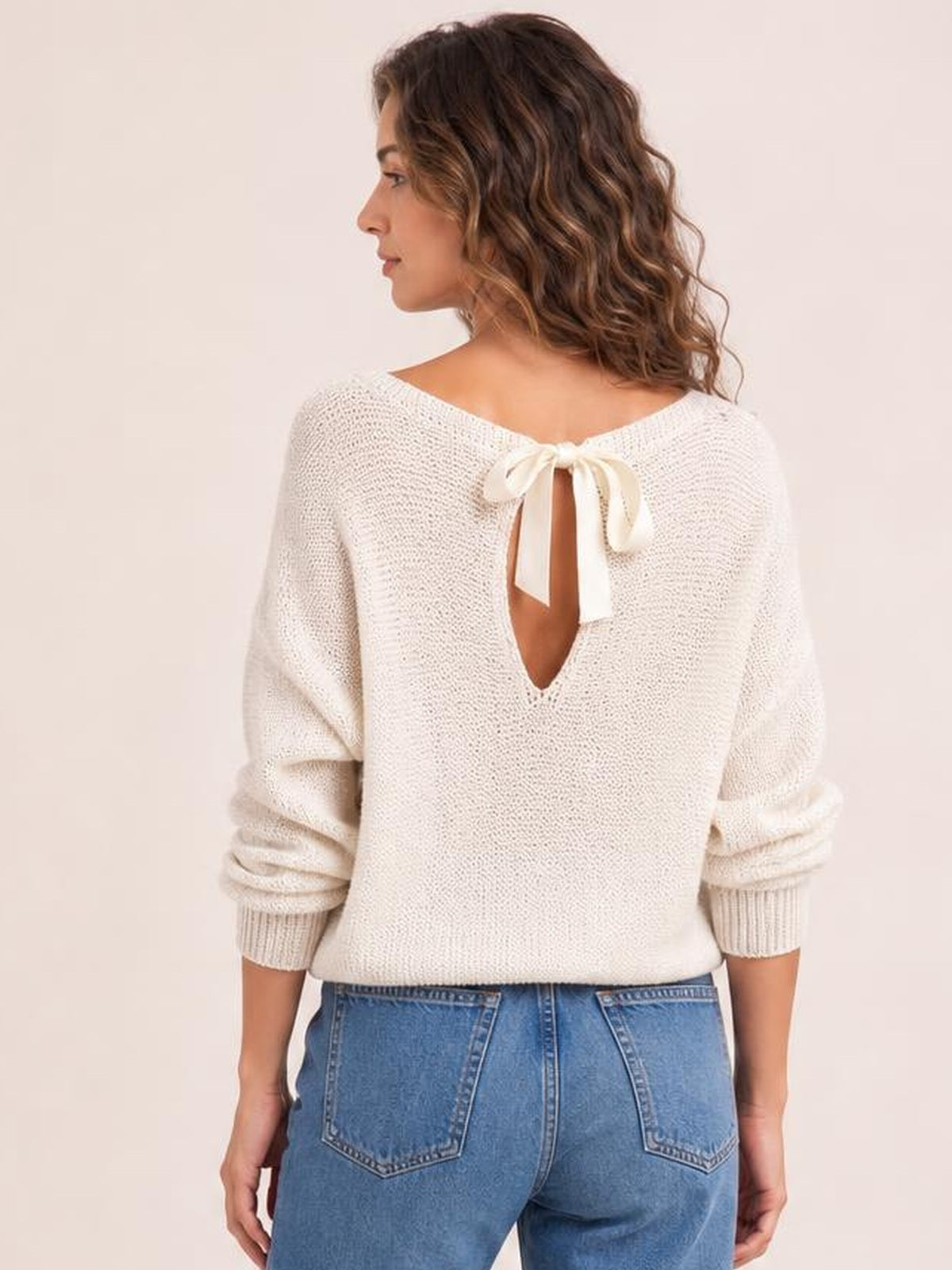 Model shown from the back wearing an ivory bow-back boat-neck sweater with batwing sleeves, a relaxed silhouette, and an open back detail.