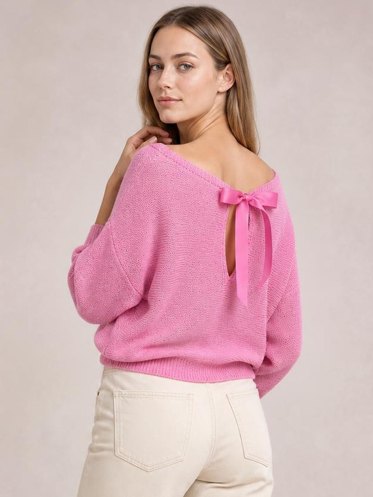 Model poses in a pink boat-neck batwing-sleeve sweater with a shoulder bow, relaxed silhouette, ribbed hem, and slight off-shoulder drape.