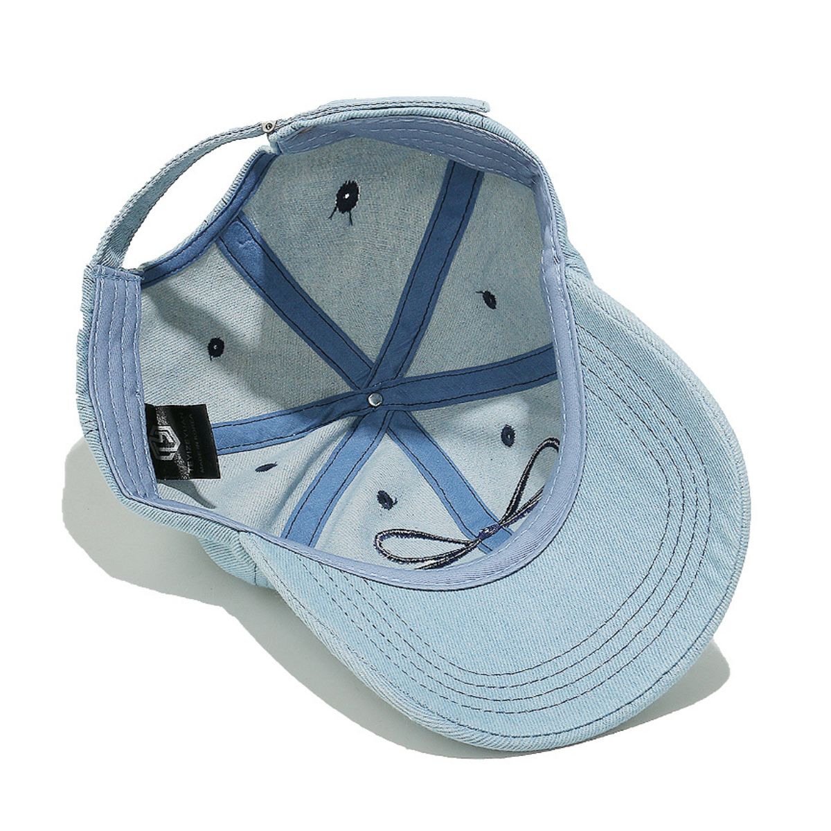 Light blue denim cotton baseball cap shown from above, featuring a classic six-panel construction, curved brim, detailed topstitching, and an embroidered bow accent.