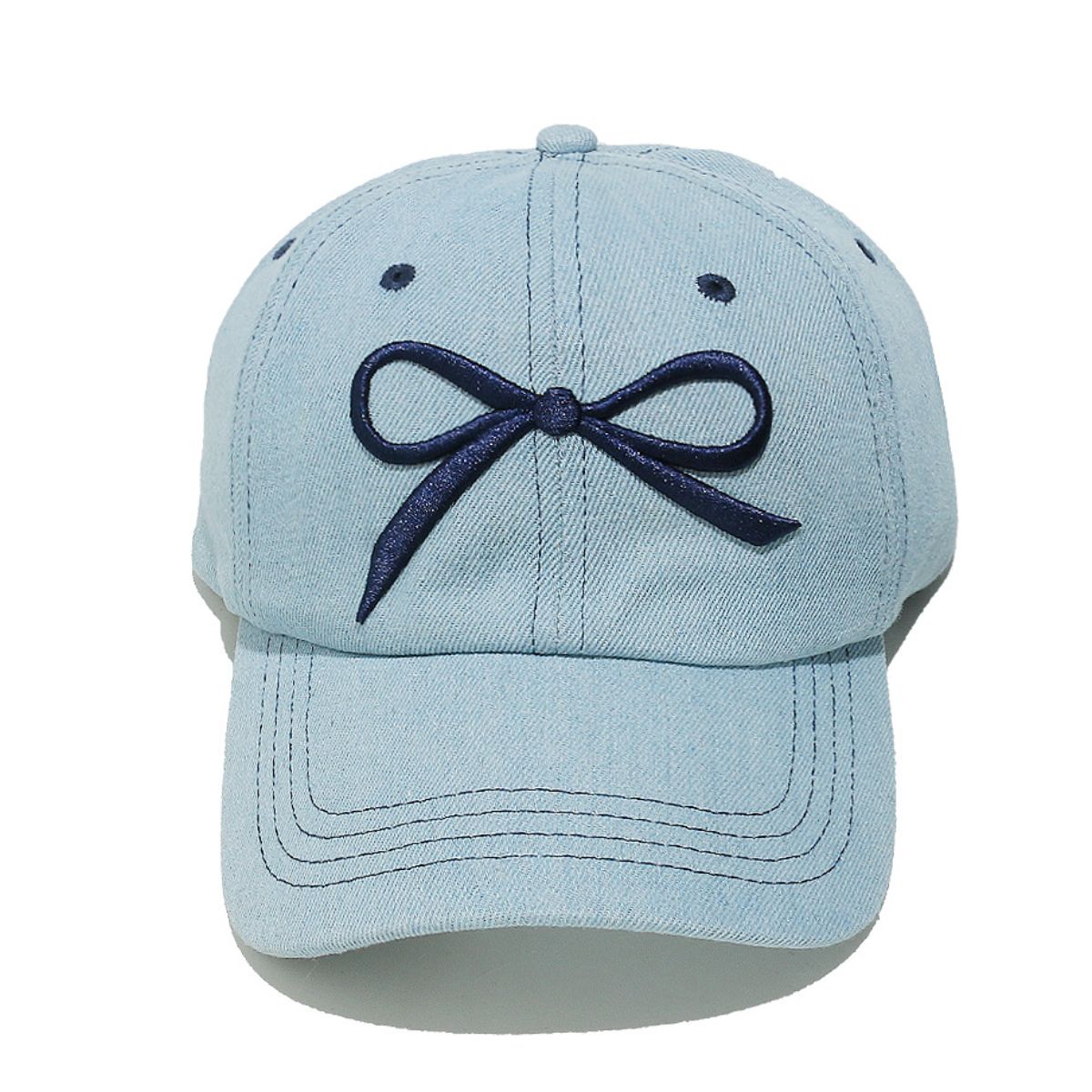 Light blue denim cotton baseball cap with a dark embroidered bow, curved brim, six-panel construction, contrast topstitching, ventilation eyelets, and crown button.