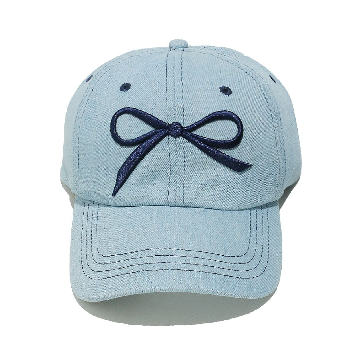 Light blue denim cotton baseball cap with a dark embroidered bow, curved brim, six-panel construction, contrast topstitching, ventilation eyelets, and crown button.