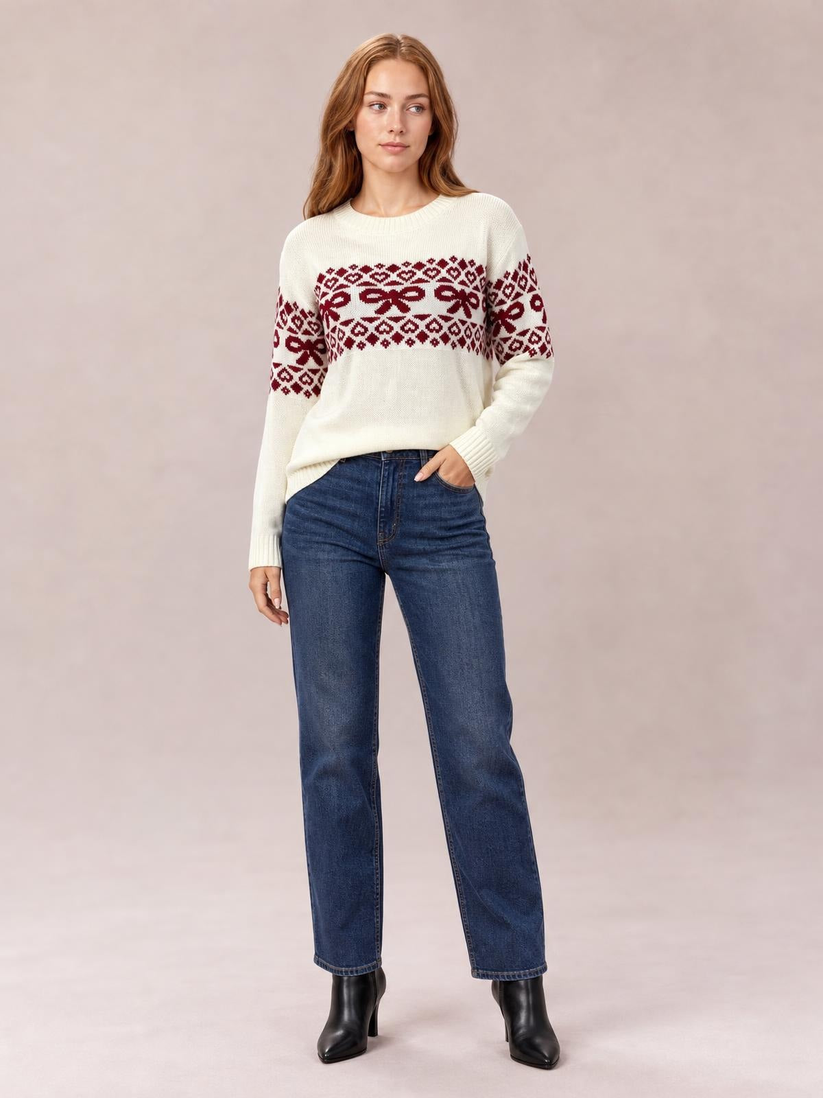 Model wearing a cream long-sleeve Christmas sweater with burgundy bow and geometric patterns, ribbed crew neck and cuffs, relaxed silhouette, standing with one hand in her pocket.