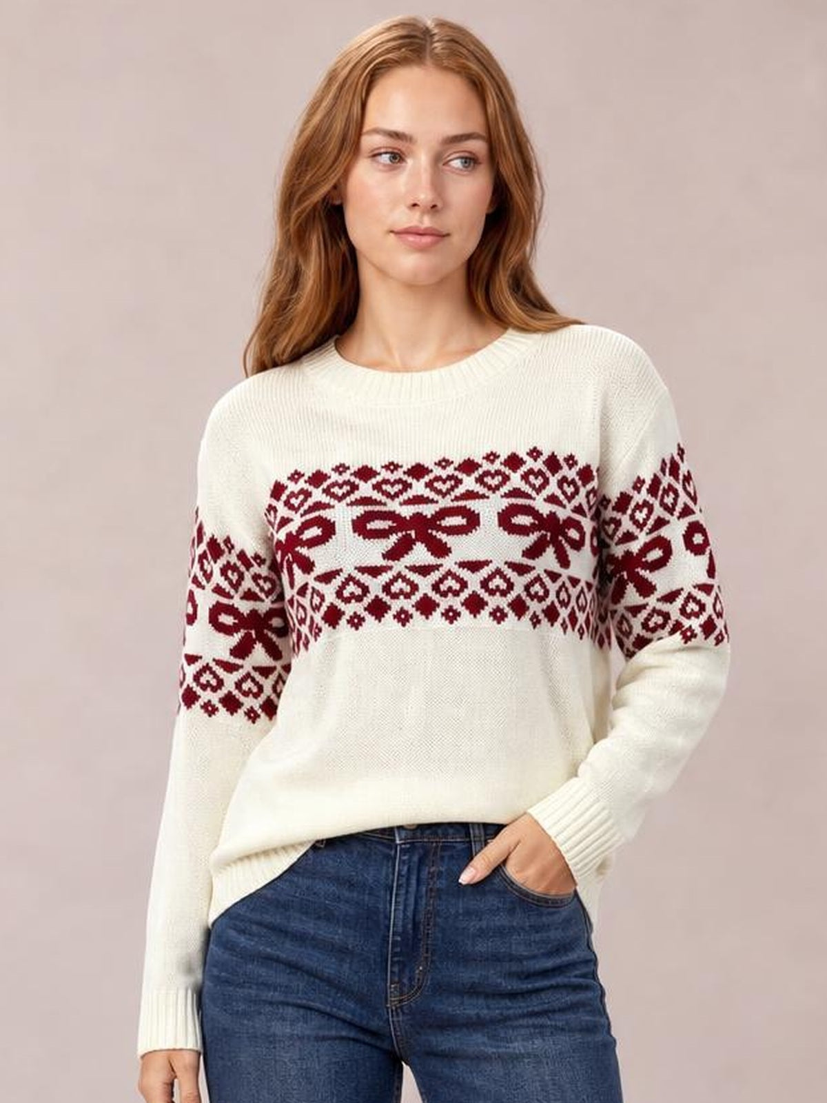Model wears an ivory long-sleeve Christmas sweater with burgundy bow and geometric patterns, a crew neckline, ribbed cuffs, and a relaxed silhouette.