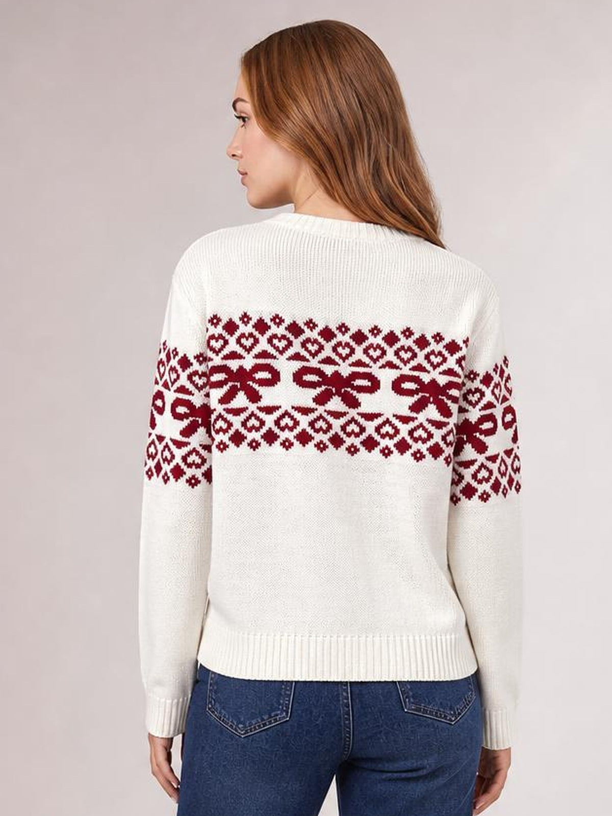 A model faces away wearing a white long-sleeve Christmas sweater with burgundy bow and geometric patterns across the back and sleeves, ribbed trim, and a fitted silhouette.