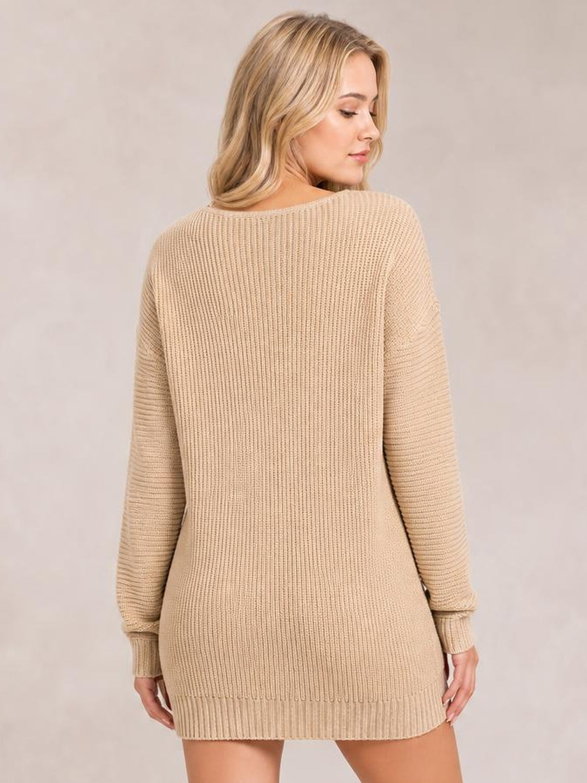 A model looks over her shoulder while wearing a beige ribbed knit sweater dress with long sleeves, a relaxed silhouette, and a ribbed hem.