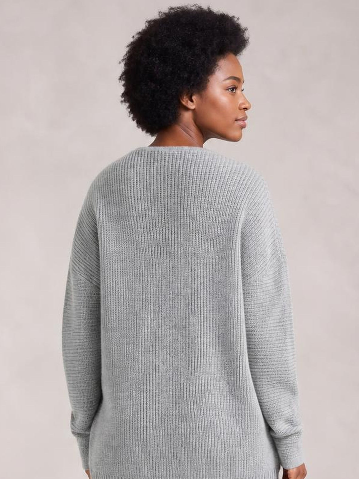 A model looks over her shoulder wearing a light gray ribbed knit sweater dress with long sleeves and a relaxed, straight silhouette.