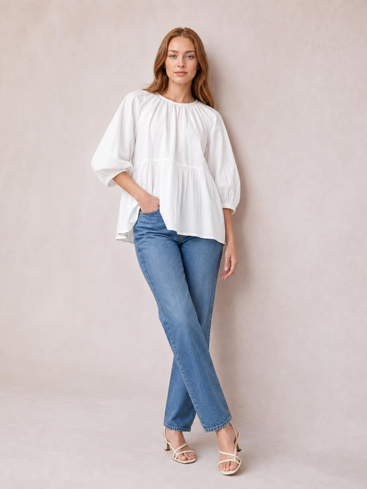 Model poses in a white round-neck blouse with three-quarter sleeves, gathered waist, and a relaxed flared silhouette.